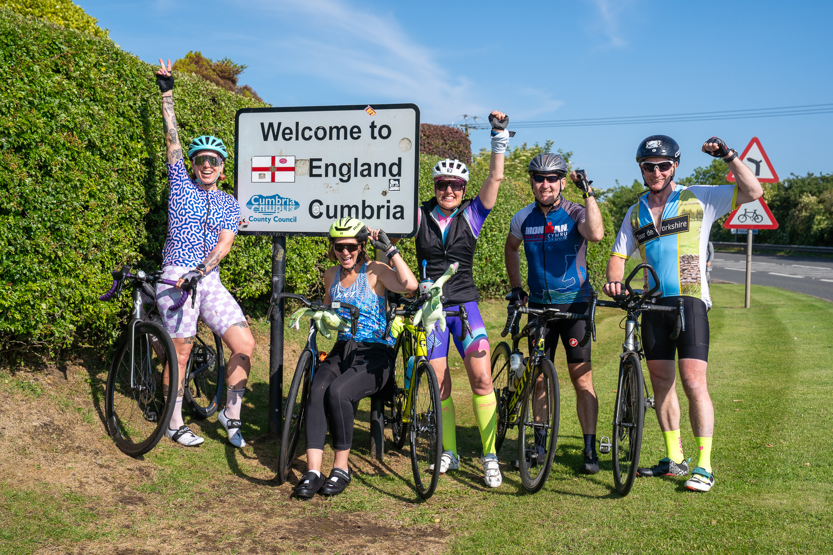 Five cyclists celebrating beside the Welcome to England sign